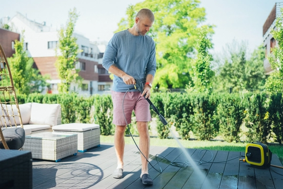 Eine Person reinigt eine Terrasse mit einem Hochdruckreiniger.